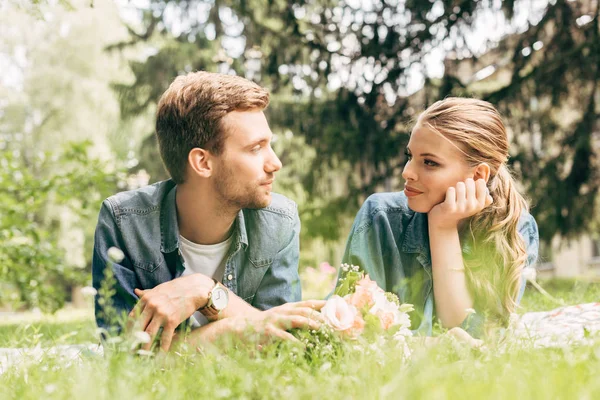 Hermosa pareja joven tumbada en la hierba en el parque y mirándose entre sí - foto de stock