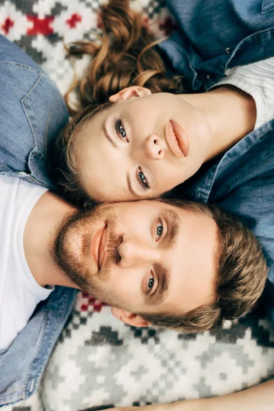 Top view of beautiful young couple lying on patterned cloth and looking at camera — Stock Photo