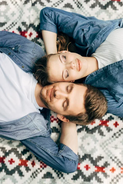 Vue de dessus de beau jeune couple couché sur un tissu à motifs avec les yeux fermés — Photo de stock