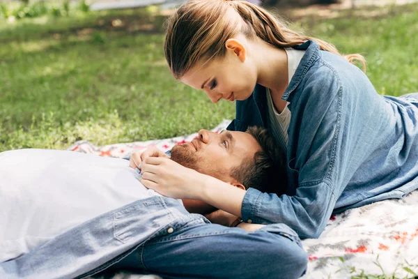 Hermosa pareja joven acostada en la hierba y coqueteando en el parque - foto de stock