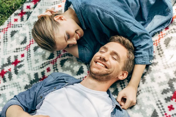 Vista de ángulo alto de feliz pareja joven acostada en tela estampada y coqueteando - foto de stock