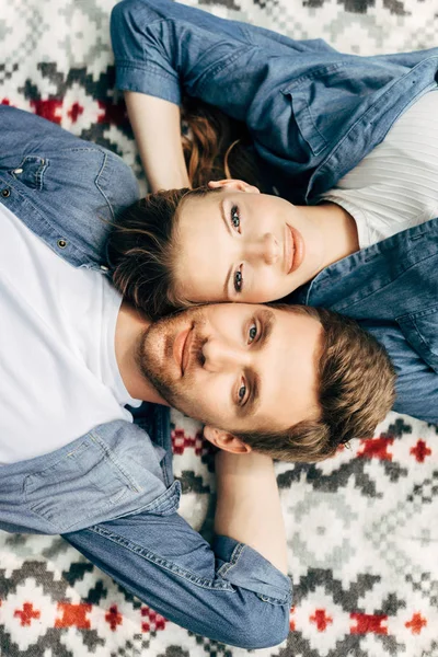 Draufsicht auf schönes junges Paar, das auf gemustertem Tuch liegt und in die Kamera blickt — Stockfoto