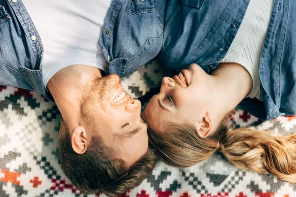 Draufsicht auf lächelndes junges Paar, das auf gemustertem Tuch liegt — Stockfoto