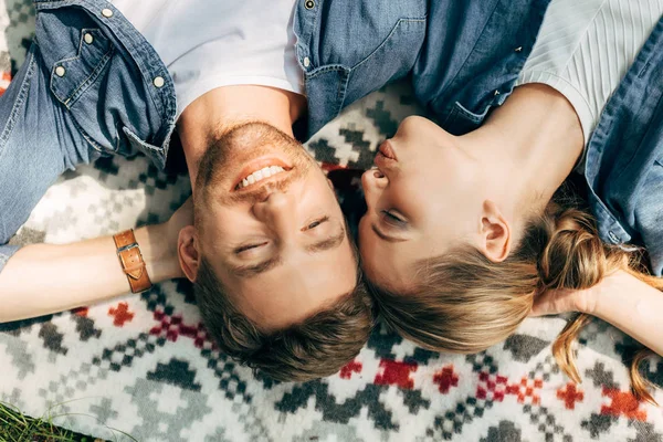 Vue de dessus du jeune couple heureux avec les yeux fermés couché sur un tissu à motifs — Photo de stock