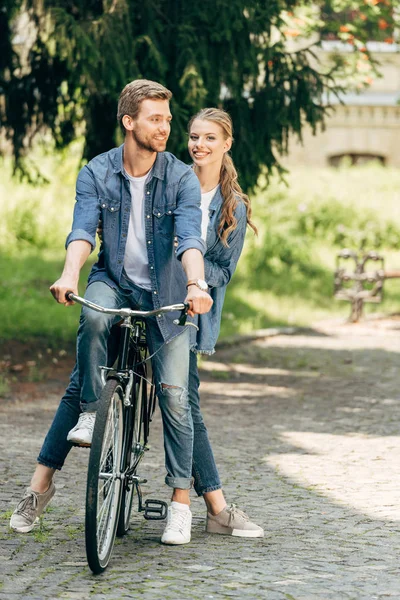 Hermosa pareja joven montar bicicleta vintage juntos en el parque - foto de stock