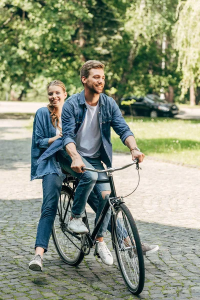 Happy young couple riding bicycle together at park — Stock Photo