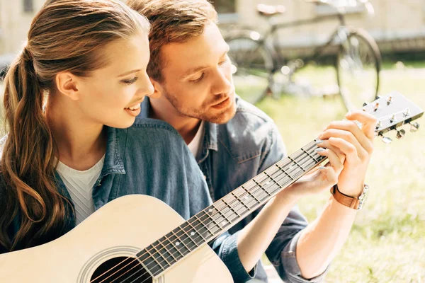 Young happy woman with boyfriend playing guitar together at park — Stock Photo