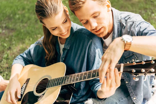 Plan rapproché de jeune femme heureuse apprenant à jouer de la guitare avec son petit ami au parc — Photo de stock