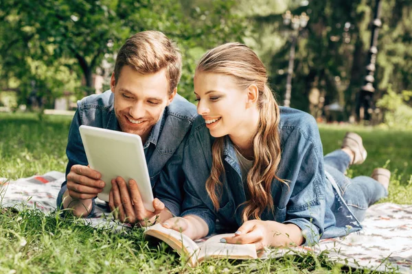 Happy young couple lying on grass at park and using tablet — Stock Photo