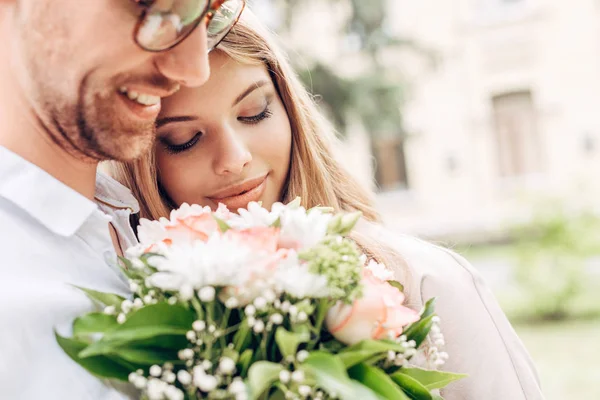 Nahaufnahme eines glücklichen jungen Paares mit Blumenstrauß, das sich im Freien umarmt — Stockfoto