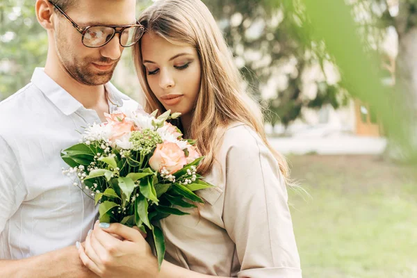 Close-up shot of stylish young couple with bouquet embracing outdoors — Stock Photo