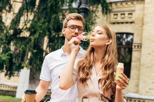 Beau jeune couple soufflant des bulles de savon ensemble en face de vieux bâtiment — Photo de stock
