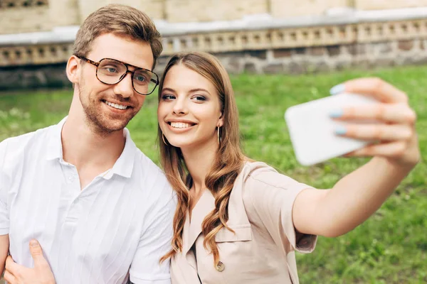 Belo jovem casal tomando selfie na frente de grama verde — Fotografia de Stock