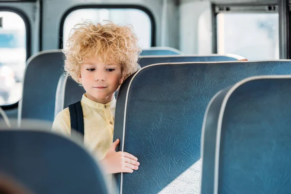 Adorable curly schoolboy standing alone in school bus — Stock Photo