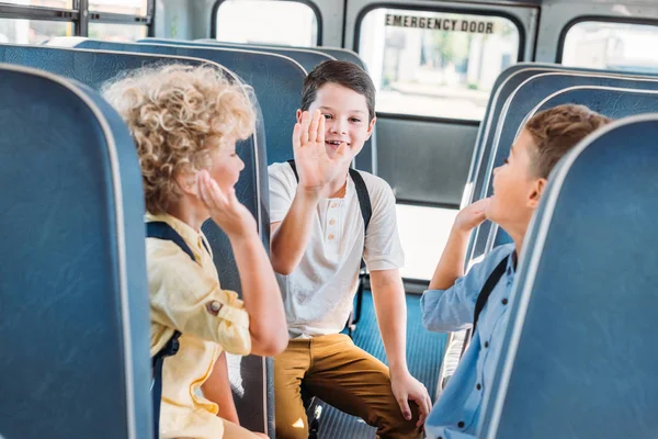 Группа очаровательных учеников, дающих пять вместе во время езды на школьном автобусе — стоковое фото