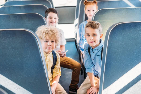 Gruppe entzückender Schüler blickt während der Fahrt im Schulbus in die Kamera — Stockfoto