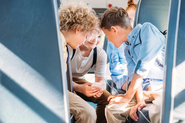 Niños pequeños y felices usando el teléfono inteligente juntos en el autobús escolar - foto de stock