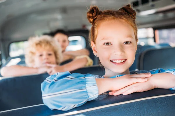 Крупним планом портрет усміхненої маленької школярки, що їде на шкільному автобусі з однокласниками позаду — стокове фото