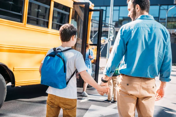 Rückansicht von Vater und Sohn beim Händchenhalten und Gehen zum Schulbus — Stockfoto