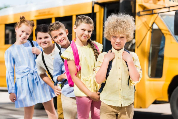 Group of happy pupils looking at camera while standing in row in front of school bus — Stock Photo