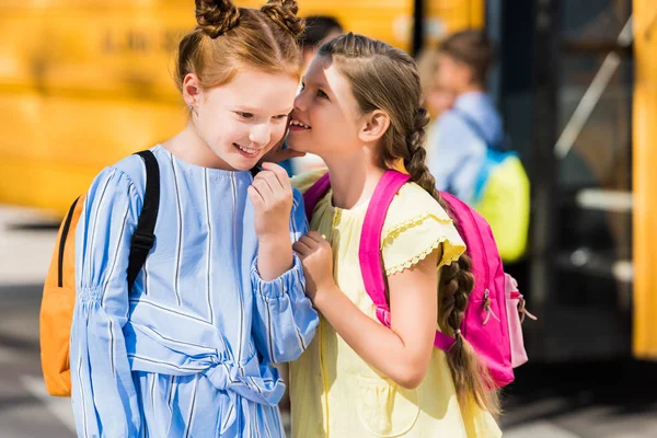 Mignonnes petites écolières bavardant devant le bus scolaire — Photo de stock