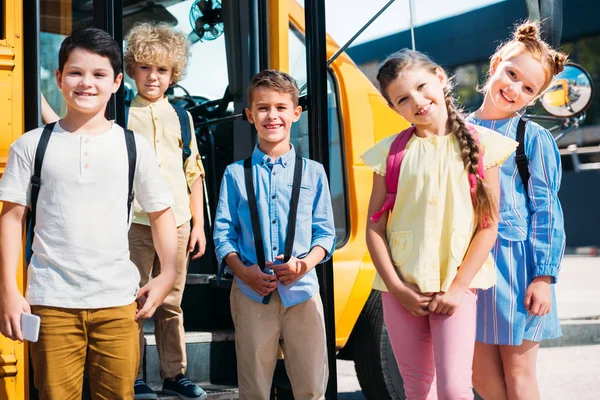 Grupo de alunos felizes olhando para a câmera na frente do ônibus escolar — Fotografia de Stock