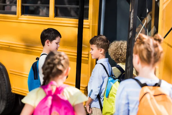 Група чарівних школярів спілкується біля шкільного автобуса — стокове фото
