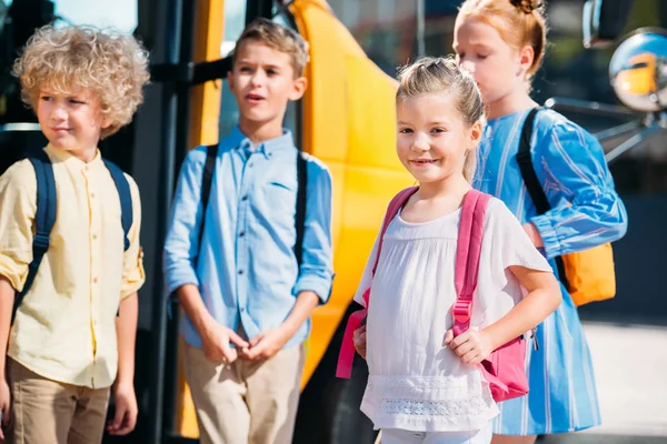 Liebenswerte Schüler, die in der Nähe des Schulbusses stehen und wegschauen — Stockfoto