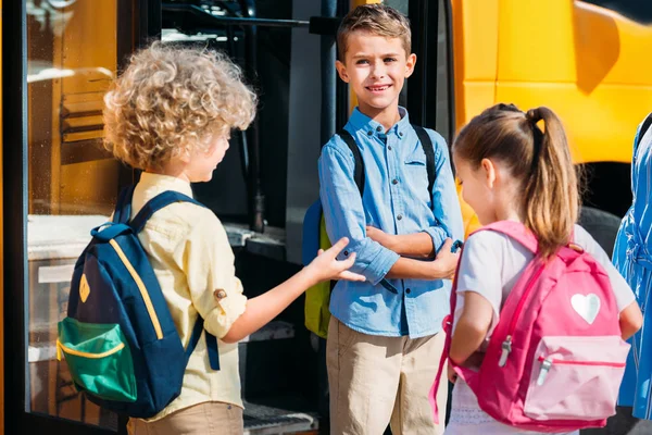 Alumnos adorables charlando cerca de autobús escolar - foto de stock