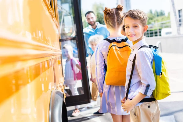 Очаровательный школьник входит в школьный автобус с одноклассниками, а учитель стоит рядом с дверью — стоковое фото