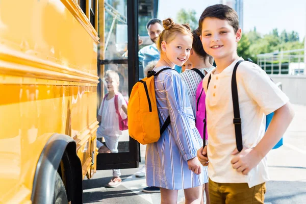 Счастливые маленькие ученики, входящие в школьный автобус с одноклассниками — стоковое фото