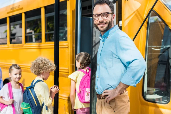 Männlicher Lehrer blickt in Kamera, während Schüler in Schulbus einsteigen — Stockfoto