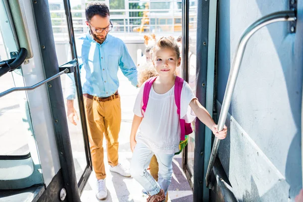 Schoolgirl entering school bus with teacher while going on excursion — Stock Photo