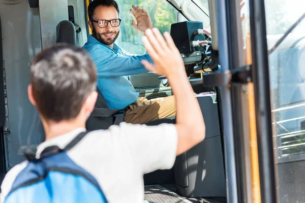 Красивый улыбающийся водитель автобуса приветствует школьника, который входит в автобус — стоковое фото