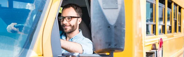 Panoramic shot of handsome school bus driver smiling and driving — Stock Photo