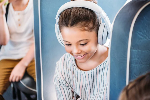 Nahaufnahme Porträt eines lächelnden Schulmädchens, das mit Kopfhörern im Bus Musik hört — Stockfoto