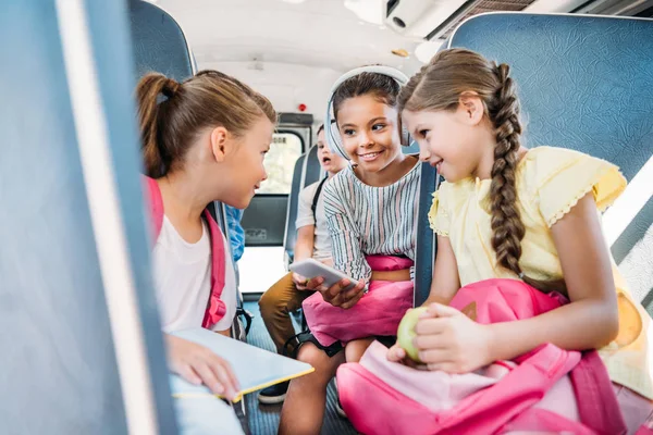 Група щасливих школярки використовують смартфон разом під час їзди на шкільному автобусі — стокове фото