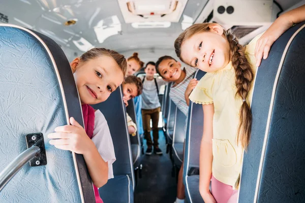 Groupe d'écoliers mignons montant sur le bus scolaire et regardant la caméra — Photo de stock