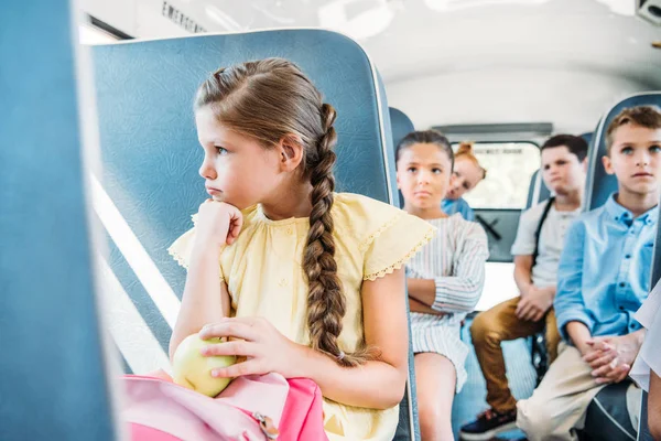 Triste piccola studentessa cavalcare su scuolabus con i suoi compagni di classe — Foto stock