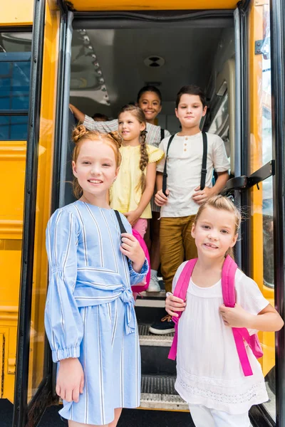 Grupo de escolares adorables de pie en el autobús escolar - foto de stock