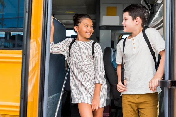 Estudiosos de pie en el autobús escolar y mirándose unos a otros - foto de stock