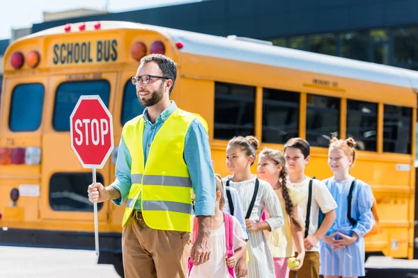 Traffic guard crossing road with schoolchildren in front of school bus — Stock Photo