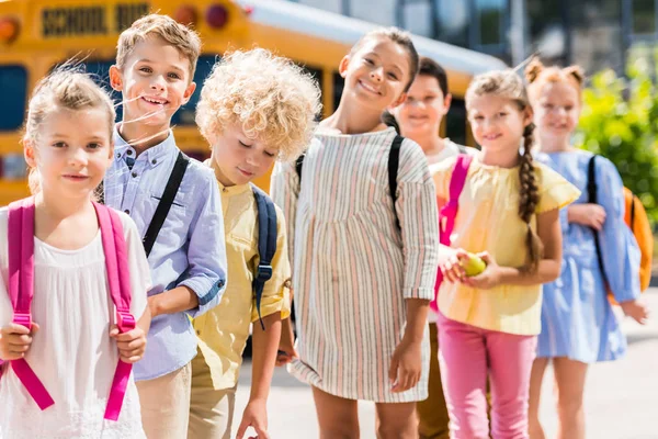 Gruppo di allievi felici in fila davanti allo scuolabus — Foto stock