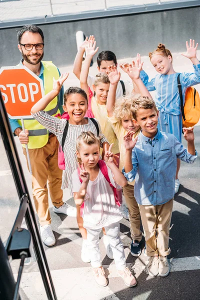 Vista da scuolabus a gruppo di studiosi con guardia del traffico guardando la telecamera e agitando — Foto stock