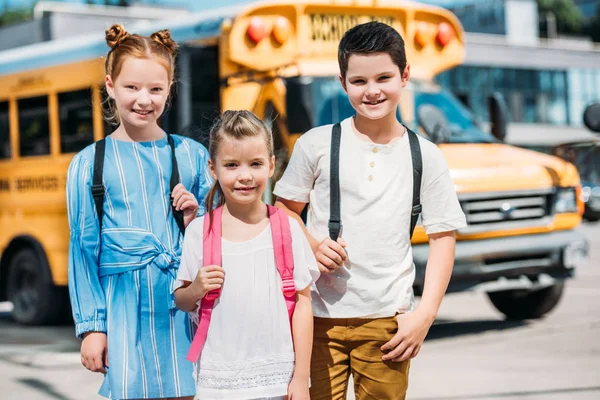 Группа улыбающихся учеников, смотрящих в камеру перед школьным автобусом — стоковое фото
