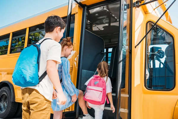 Vista trasera de los alumnos con mochilas que entran en el autobús escolar - foto de stock