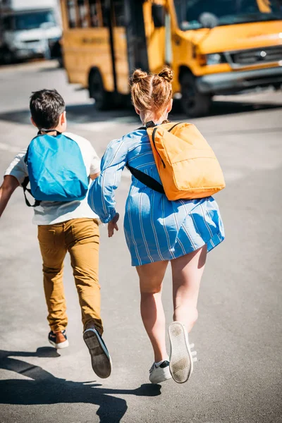 Vista posteriore degli alunni con zaini in corsa verso lo scuolabus — Foto stock