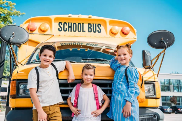 Groupe d'adorables élèves penchés sur le bus scolaire et regardant la caméra — Photo de stock