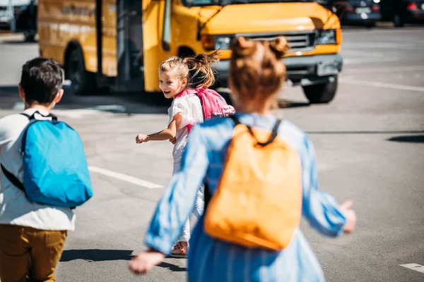 Visão traseira de crianças felizes escolares correndo para o ônibus escolar — Fotografia de Stock