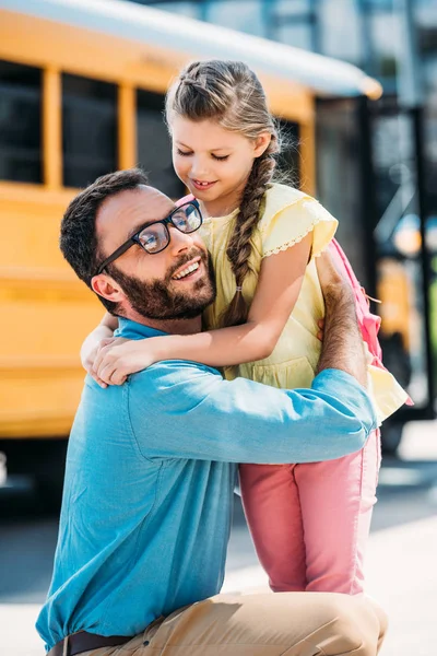 Щасливий батько обіймає свою маленьку доньку перед шкільним автобусом — стокове фото